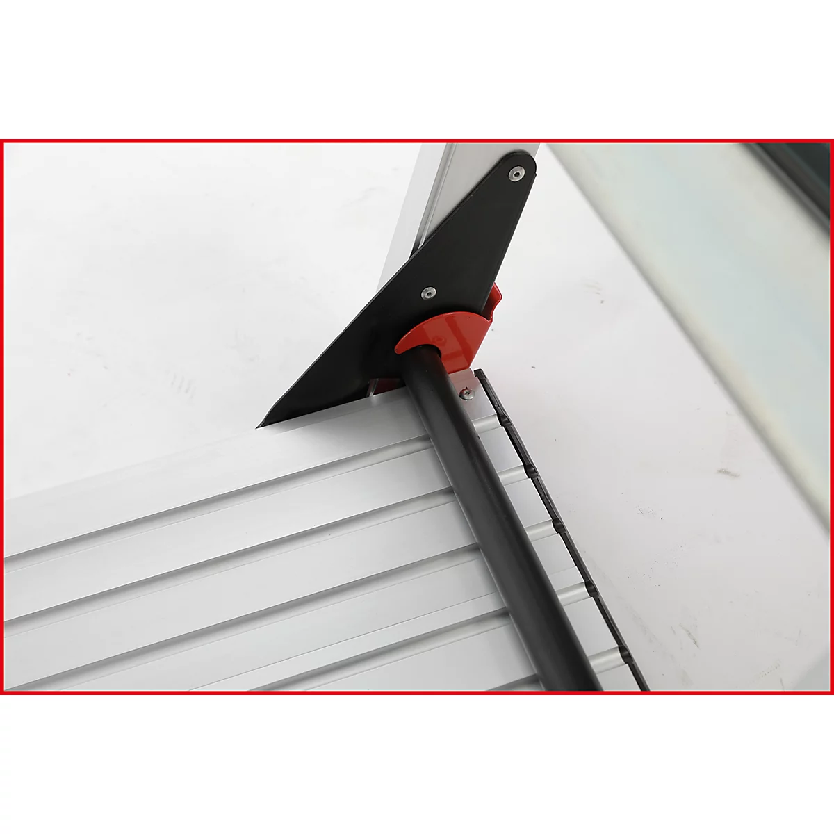 Detailaufnahme eines schwarzen und roten Werkzeugs an einer weißen Oberfläche mit metallischen Leisten.